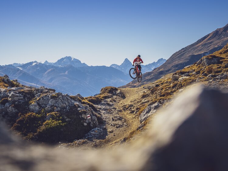 Ein Biker macht einen Sprung auf dem Signaltrail auf Gotschna, das Tinzenhorn im Hintergrund.  | © Davos Klosters Mountians