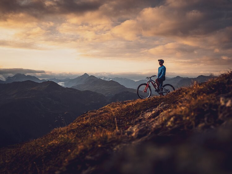 Ein Biker sitzt bei Sonnenuntergang auf seinem Bike und blickt in die Ferne. | © Davos Klosters Mountains