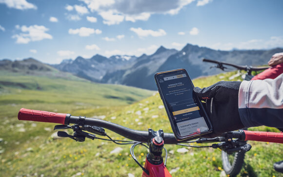 Biker hält das Handy in seiner Hand und bucht über den Webshop sein Begrbahnticket für das Bike. | © Davos Klosters Mountains