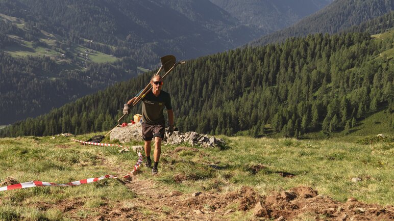 Christoph Koch, Mitglied der Trail Crew Davos, ist mit Rechen und Schaufel über der Schulter auf dem Berg unterwegs.  | © Carmen Wenger / Destination Davos Klosters