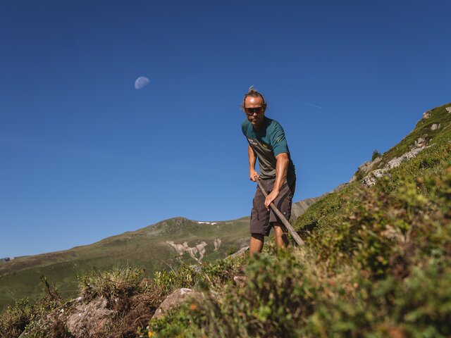 Mond Trail Crew Davos | © Carmen Wenger / Destination Davos Klosters Ein Mitglied der Trail Crew Davos verbessert mit der Schaufel den Weg, am blauen Himmel der Mond. | © Carmen Wenger / Destination Davos Klosters