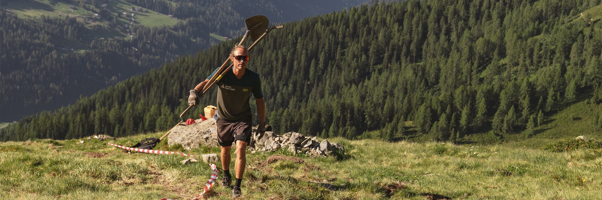 Trail Crew Davos in Aktion | © Carmen Wenger / Destination Davos Klosters Christoph Koch, Mitglied der Trail Crew Davos, ist mit Rechen und Schaufel über der Schulter auf dem Berg unterwegs. | © Carmen Wenger / Destination Davos Klosters
