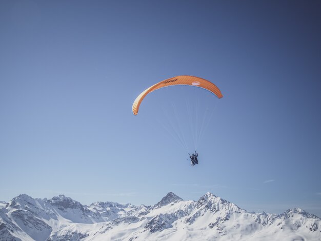 Ein Gleitschirmflieger geniesst den Flug vor einem verschneiten Bergpanorama.  | © Davos Klosters Mountains