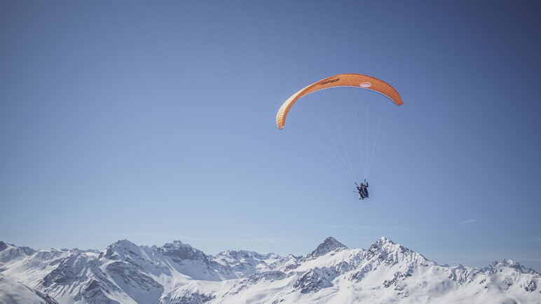 Ein Gleitschirmflieger geniesst den Flug vor einem verschneiten Bergpanorama.  | © Davos Klosters Mountains