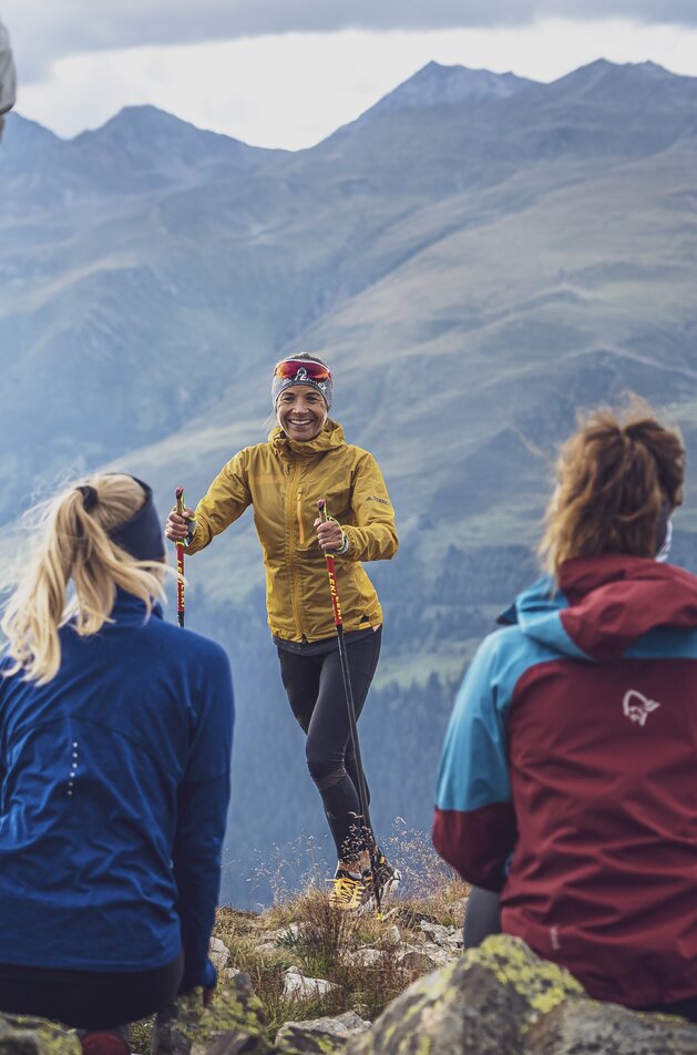 Die drei Läuferinnen sitzen auf dem Felsen mit dem Blick zur Trainerin  Jasmin Nunige. | © Davos Klosters Mountains