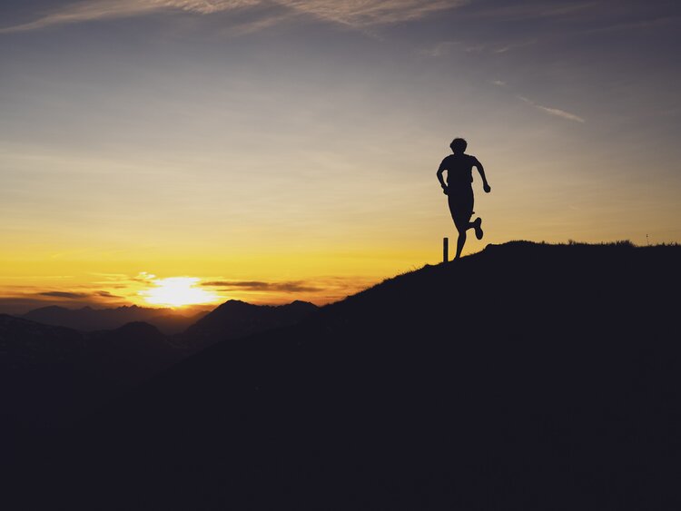 Silhouette eines Trailrunners auf dem Grat vom Berg Jakobshorn, der in Richtung Sonnenuntergang rennt.  | © Davos Klosters Mountains