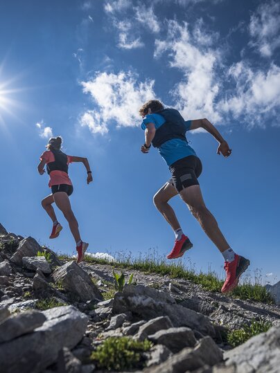 Zwei Trailrunner rennen im Gleichschritt und mit viel Körperspannung dem Berg hinauf in Richtung der scheinenden Sonne.  | © Davos Klosters Mountains