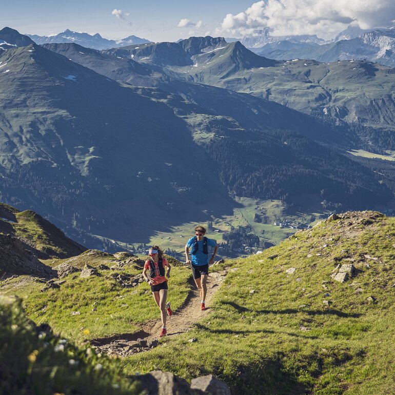 Ein Trailrunning Paar rennt auf dem Grat auf dem Jakobshorn, im Hintergrund im Tal ist der Davosersee ersichtlich.  | © Davos Klosters Mountains