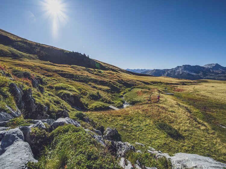 Ein Trailrunning Paar rennt über die grüne Ebene auf Madrisa bei sonnigem Wetter.  | © Davos Klosters Mountains