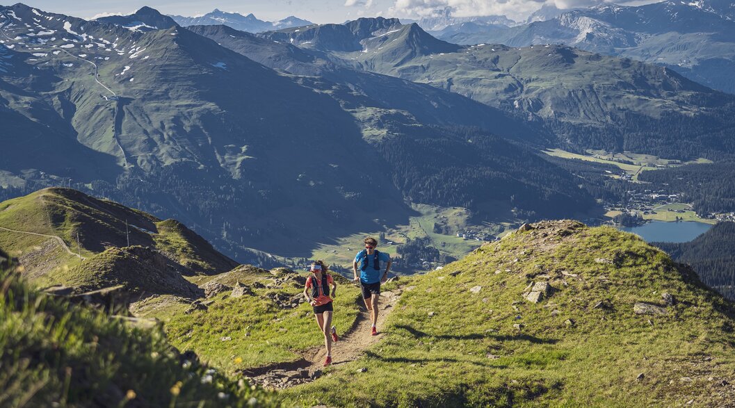 Trailrunning Jakobshorn Blick Davosersee | © Davos Klosters Mountains Ein Trailrunning Paar rennt auf dem Grat auf dem Jakobshorn, im Hintergrund im Tal ist der Davosersee ersichtlich. | © Davos Klosters Mountains