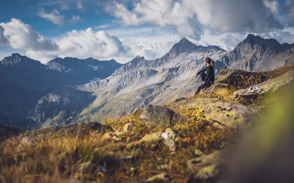 Trailrunnerin geniesst ihre Pause auf einem Stein und schaut in die Bergen. | © Davos Klosters Mountains