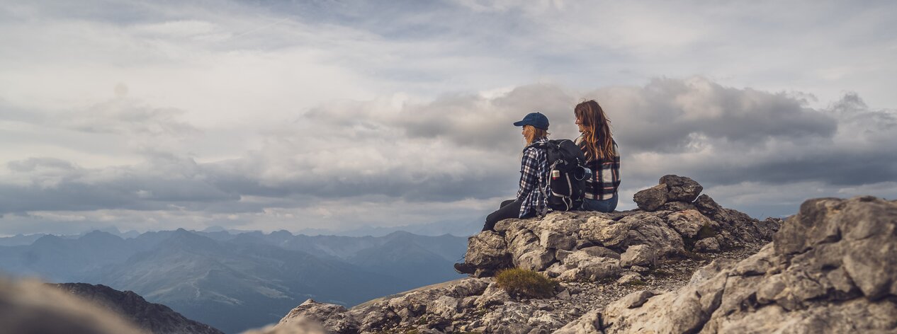 Wanderfreundinnen geniessen die Aussicht auf einem Stein. | © Davos Klosters Moutains