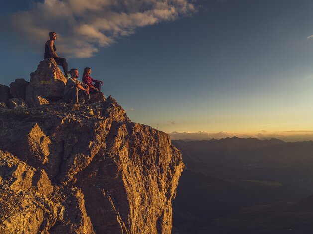 Drei Wanderer geniessen den Sonnenuntergang in den Davos Klosters Mountains. | © Davos Klosters Mountains