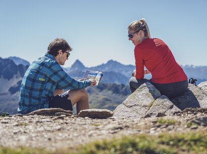Mit einem schönen Bergpanorama geniesst ein Paar die Pause der Wanderung, der Mann mit der Karte in der Hand erklärt der Frau die Wanderroute.  | © Davos Klosters Mountains