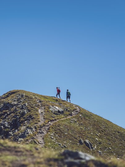 In der Ferne wandert ein Paar auf dem Grat des Jakobshorns in Richtung des Jatzhorns und geniesst den wolkenlosen Himmel.  | © Davos Klosters Mountains
