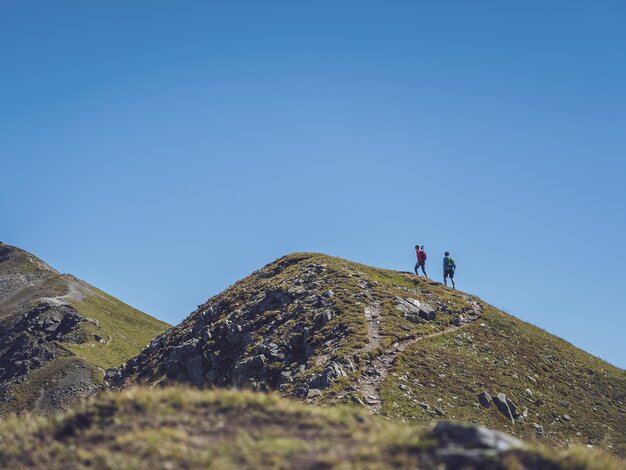 In der Ferne wandert ein Paar auf dem Grat des Jakobshorns in Richtung des Jatzhorns und geniesst den wolkenlosen Himmel.  | © Davos Klosters Mountains
