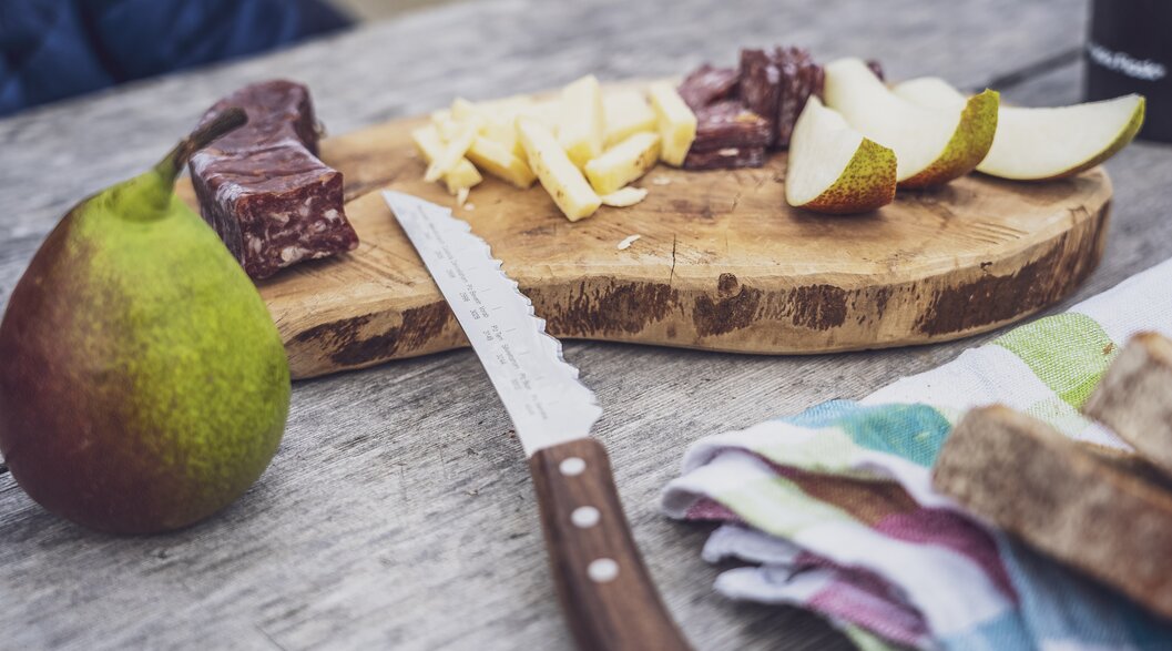 As a snack on the hike there are prepared sliced sausage, cheese and fruits on a wooden board. | © Davos Klosters Mountains