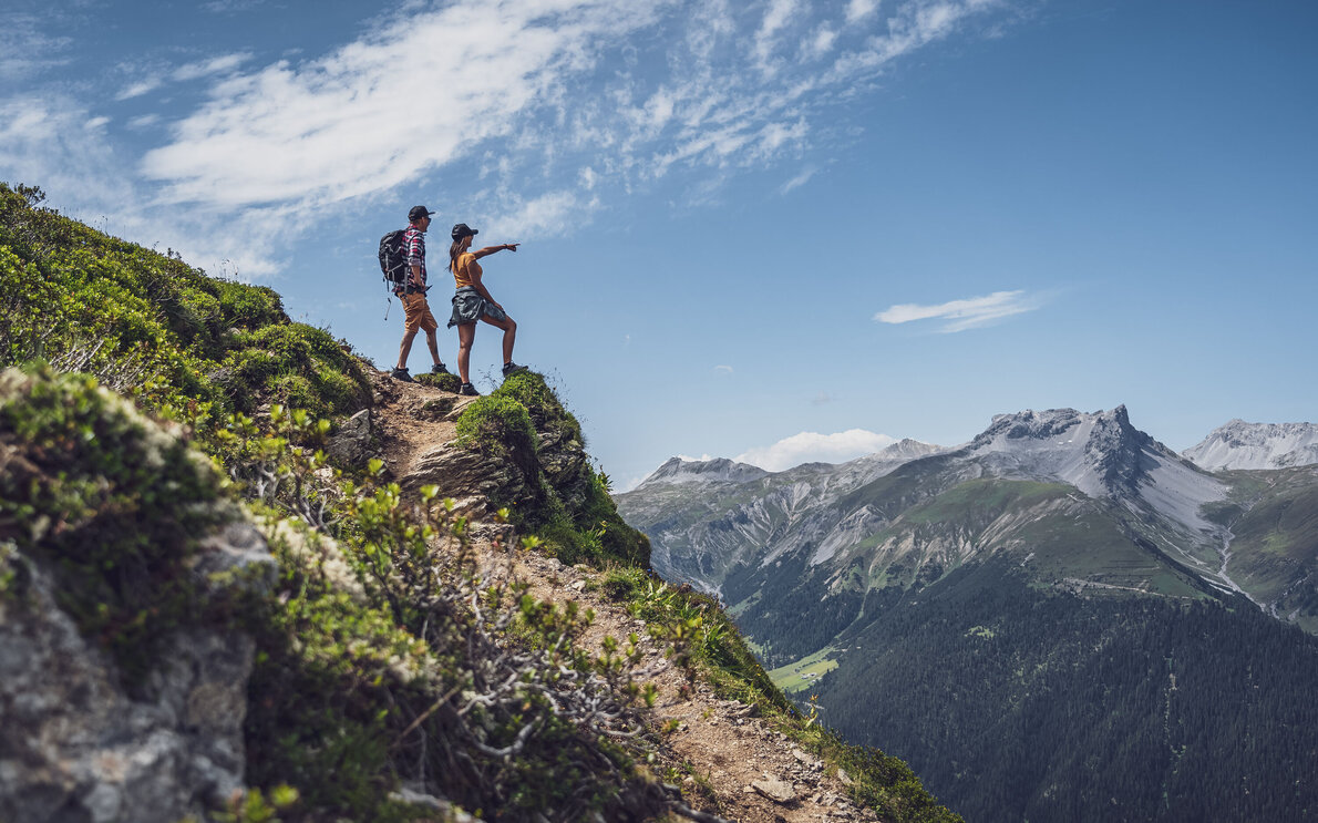 Mann und Frau stehend auf einem Felsen, sie schauen in die Ferne  | © Davos Klosters Mountains 