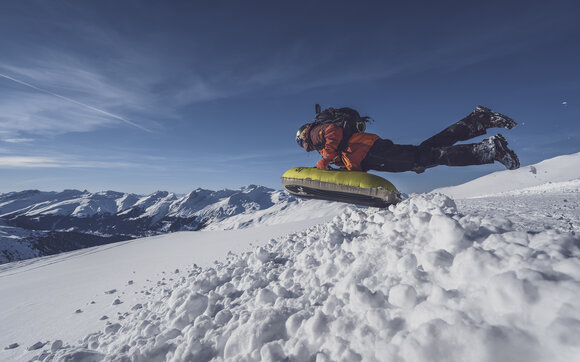 Mit einem Sprung startet ein Gast die Abfahrt über die verschneiten Hänge auf Pischa. | © Davos Klosters Mountains