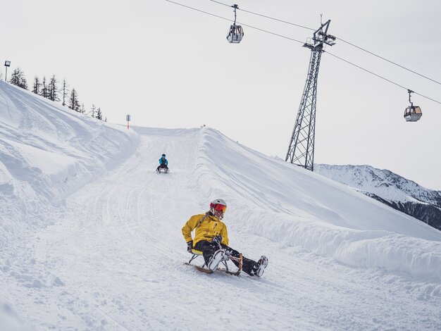 Zwei Freundinnen schlitteln auf der Schlittelstrecke Rinerhorn um eine der 24 Kurve mit der Rinerhornbahn im Hintergund. | © Davos Klosters Mountains
