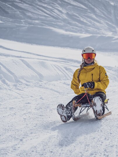 Zwei Freundinnen in farbiger Winterkleidung schlitteln auf der Schlittelstrecke Rinerhorn ins Tal. | © Davos Klosters Mountains