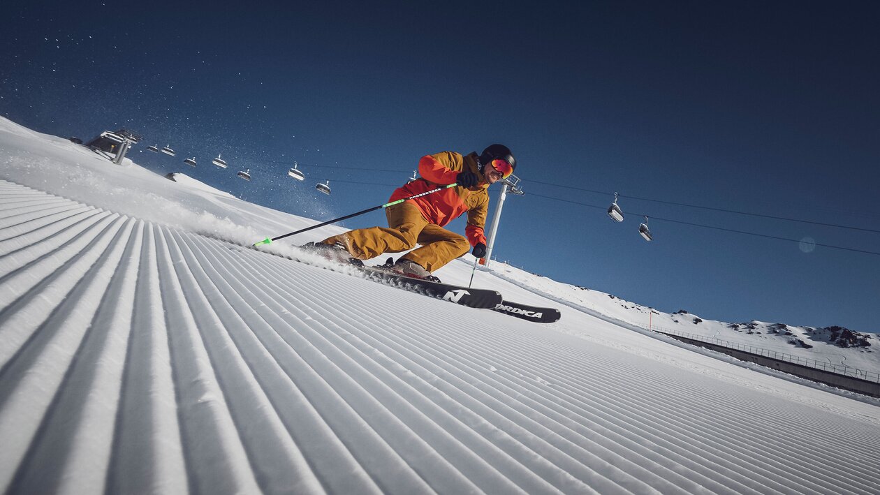 Ein Skifahrer am carven vor der Liftanlage auf einer perfekt präparierten Piste in der Sonne | © Davos Klosters Bergbahnen AG