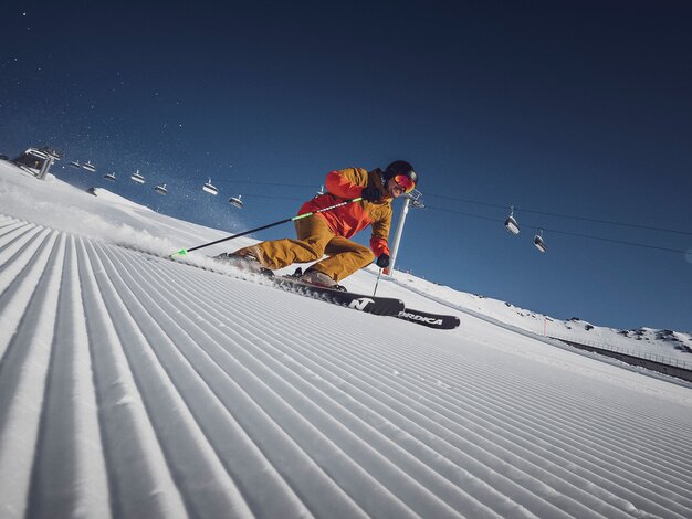 Ein Skifahrer am carven vor der Liftanlage auf einer perfekt präparierten Piste in der Sonne | © Davos Klosters Bergbahnen AG