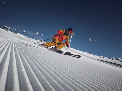 Ein Skifahrer am carven vor der Liftanlage auf einer perfekt präparierten Piste in der Sonne | © Davos Klosters Bergbahnen AG