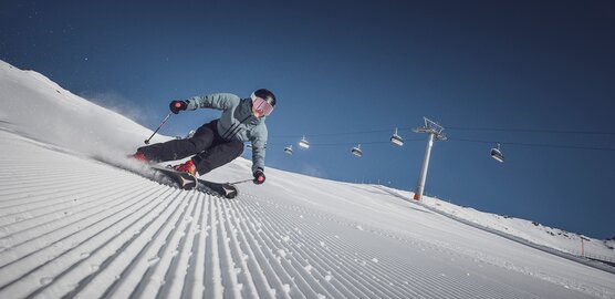 Eine Skifahrerin am carven vor der Liftanlage auf einer perfekt präparierten Piste in der Sonne