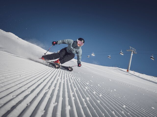 Eine Skifahrerin am carven vor der Liftanlage auf einer perfekt präparierten Piste in der Sonne | © Davos Klosters Bergbahnen AG