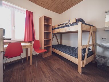 Zimmer mit Stockbett, Kleiderablage, Lavabo und Schreibtisch mit Stuhl | © Davos Klosters Mountains 