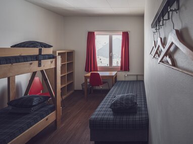 Einfaches Zimmer mit Stockbett, Zusatzbett und Kleiderablage | © Davos Klosters Mountains