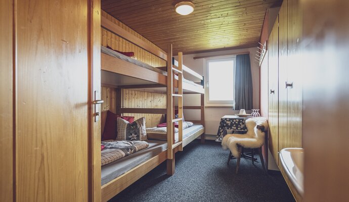 Multi-bed room with bunk beds, washbasin, table and chair  | © Davos Klosters Mountains 