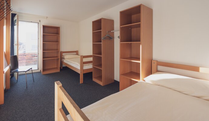 Einfaches Mehrbettzimmer mit Bettwäsche und Kleiderablagen | © Davos Klosters Mountains 