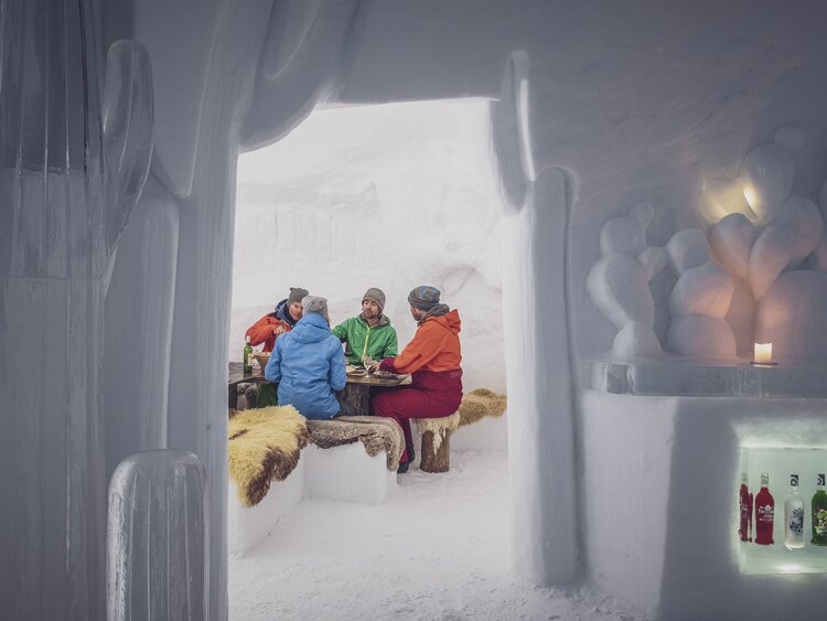 Schnee Iglu mit mehreren Personen sitzend auf Lammfell, am Fondueessen  | © Davos Klosters Mountains 