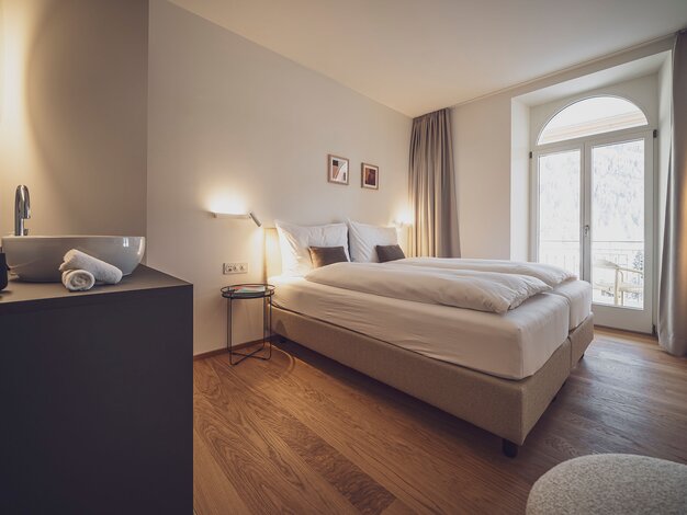 Zimmer mit Doppelbett, Holzboden und Nachttischlampen  | © Davos Klosters Mountains 