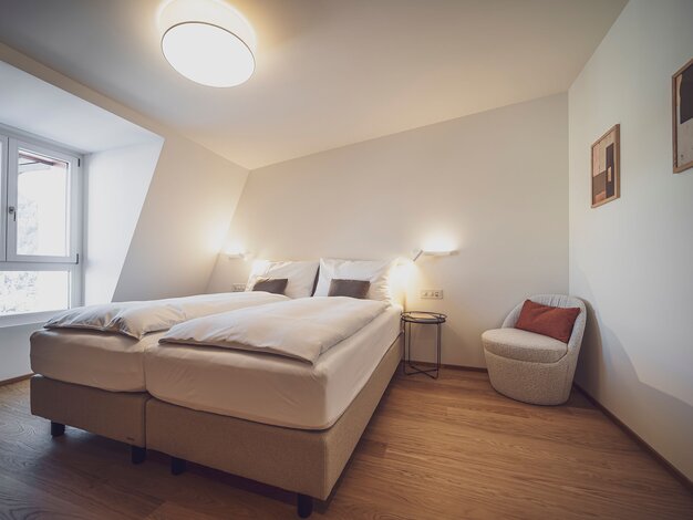 Zimmer mit Dachschräge, Doppelbett und Sitzgelegenheit | © Davos Klosters Mountains 
