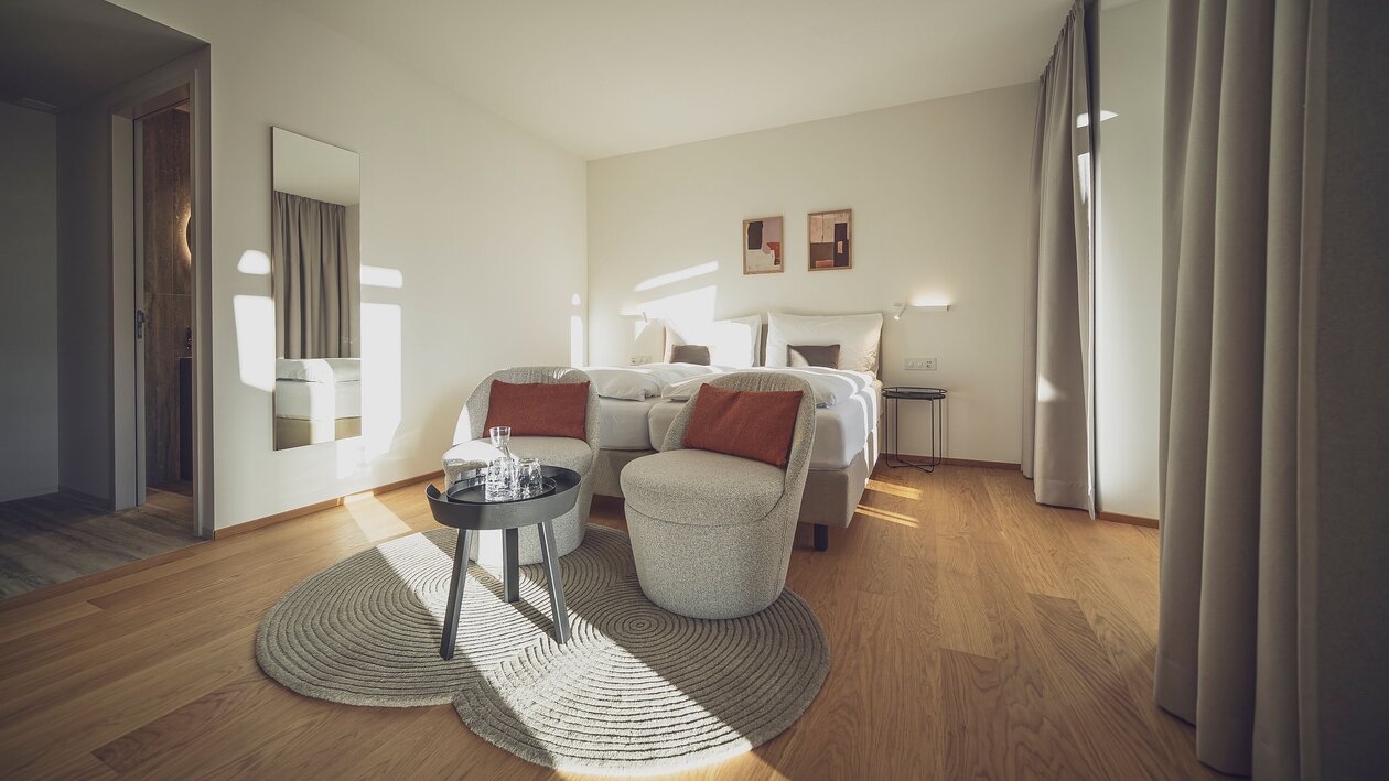 Helles Doppelzimmer mit Holzboden, Salontisch und Sitzgelegenheiten | © Davos Klosters Mountains 