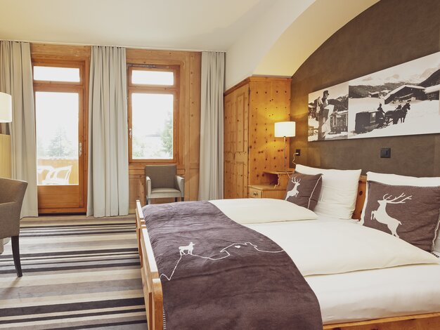 Doppelbettzimmer mit Bettwäsche im Hirschstyle, Fenster mit Stuhl und Holzeinrichtung | © Davos Klosters Mountains 