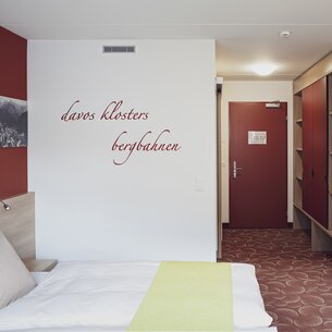 Roter Schriftzug ziert ein Doppelzimmer im Hotel Ochsen 2 passend zu Wände und Teppich.  | © Davos Klosters Mountains