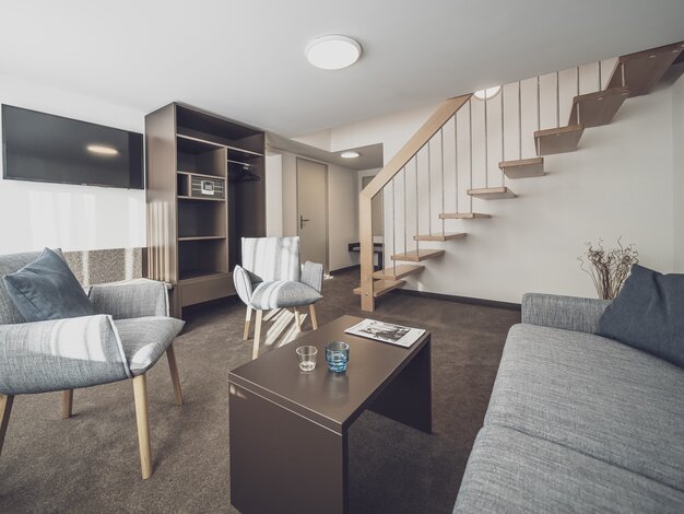 Wohnzimmer mit Sofa und Holztreppe nach oben | © Davos Klosters Mountains