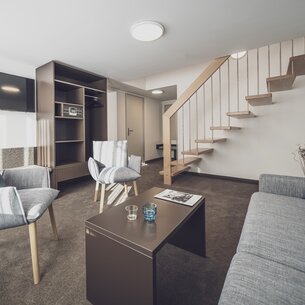 Wohnzimmer mit Sofa und Holztreppe nach oben | © Davos Klosters Mountains