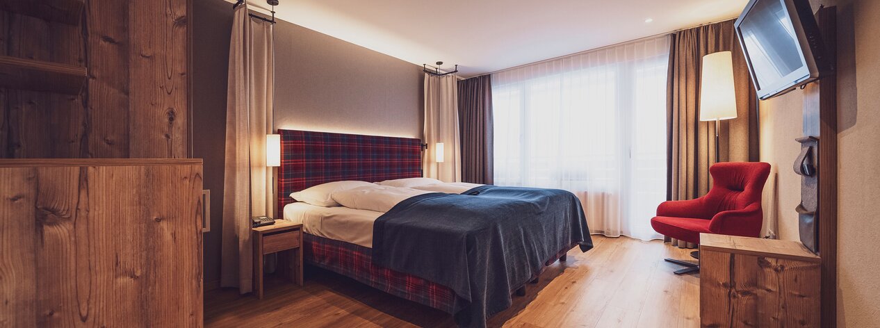 Doppelbettzimmer mit Balkon, klassischer Arveneinrichtung, Lounchsessel, Kommode und Holzboden | © Davos Klosters Mountains 