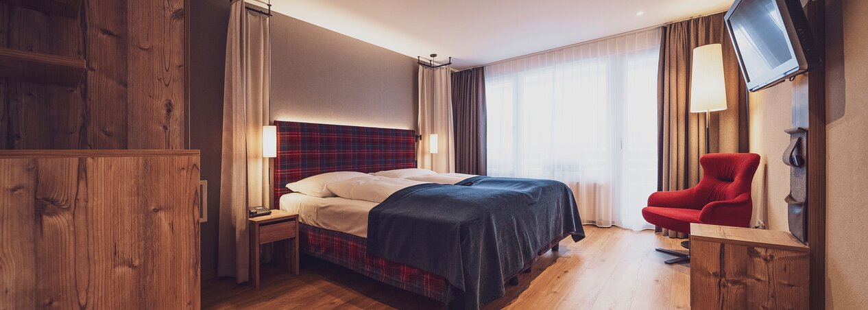 Doppelbettzimmer mit Balkon, klassischer Arveneinrichtung, Lounchsessel, Kommode und Holzboden | © Davos Klosters Mountains 