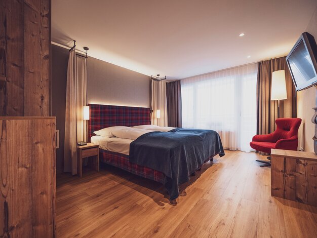 Doppelbettzimmer mit Balkon, klassischer Arveneinrichtung, Lounchsessel, Kommode und Holzboden | © Davos Klosters Mountains 