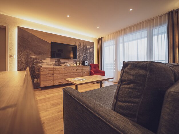 Grosses Zimmer mit Holzboden, Sofa, Holzkommode und Fernseher | © Davos Klosters Mountains 