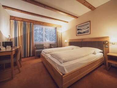 Doppelbettzimmer mit grossen Fenstern, Vorhängen und Teppichboden  | © Davos Klosters Mountains 