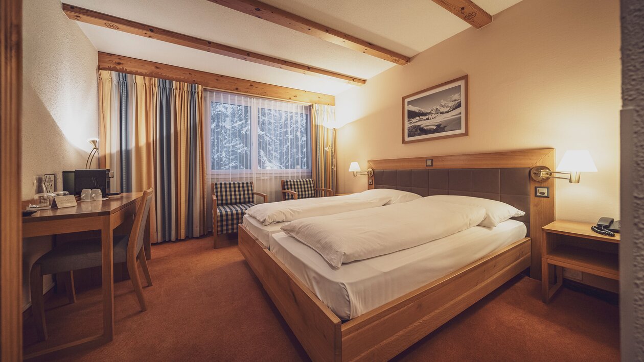 Doppelbettzimmer mit grossen Fenstern, Vorhängen und Teppichboden  | © Davos Klosters Mountains 