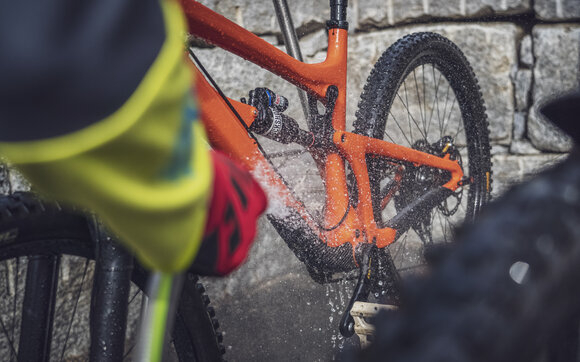Das orange Mountainbike wird mit dem Wasserstrahl sauber gewaschen. | © Davos Klosters Mountains