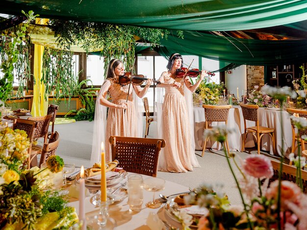 Zwei Geigerinnen im wunderschön dekorierten Ballsaal des Hotel Waldhuus Davos mit vielen bunten Blumen-Bouquets | © The Tailors Photography | Julia Schneider-Reissle